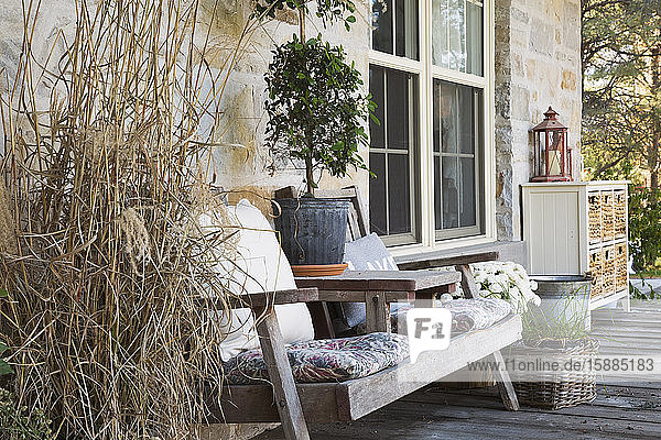 Outdoor deck with wooden chairs plant pots with plants and honey coloured stone house.