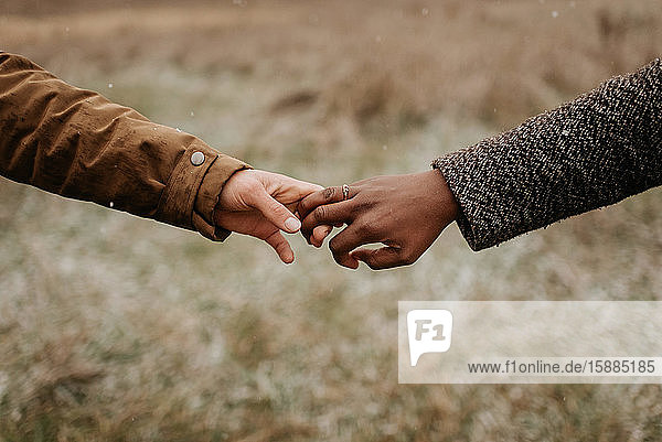 Interracial couple man and woman holding hands one wearing a gold wedding ring.