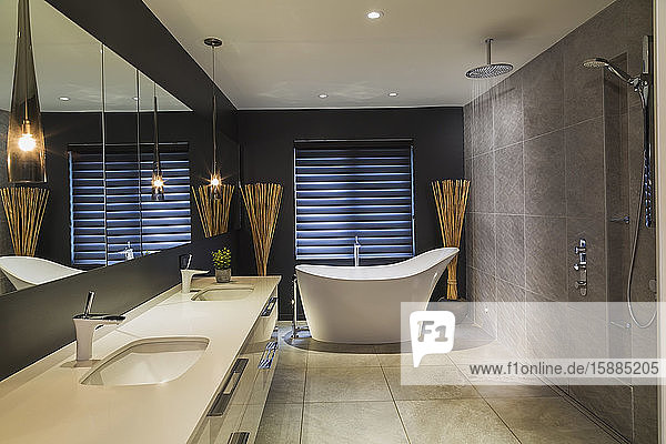 Bathroom with cream tiled floor brown tiled walls cream double hand basin and white standalone bath.