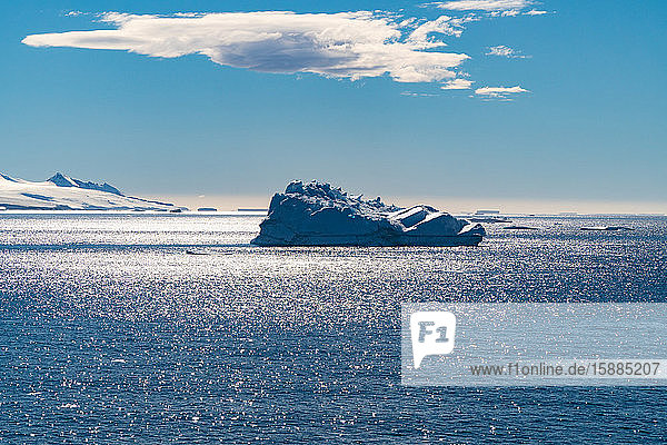An iceberg floating in the Southern Atlantic Ocean below a blue sky with a cloud.