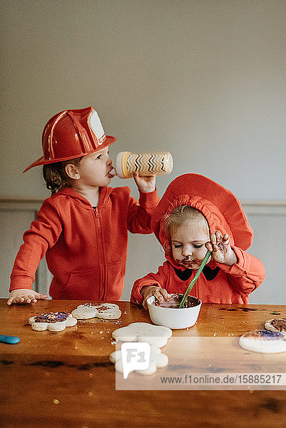 Two children dressed as firefighters at a table decorating cookies with chocolates and sprinkles.