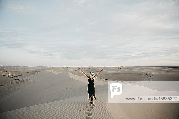 Rückenansicht einer blonden Frau  die auf einer Sanddüne steht und die Hände hebt  Algodones Dunes  Brawley  USA