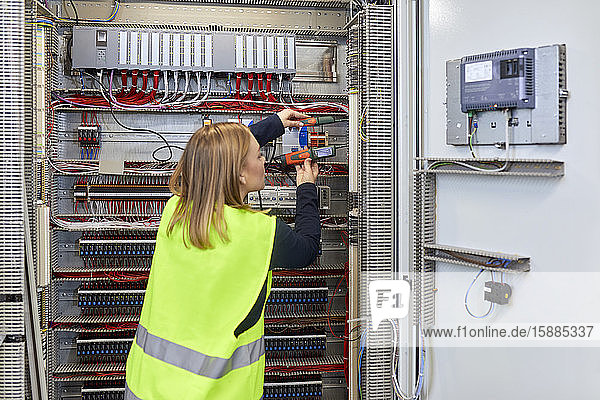 Female electrician working with voltmeter at fuse box