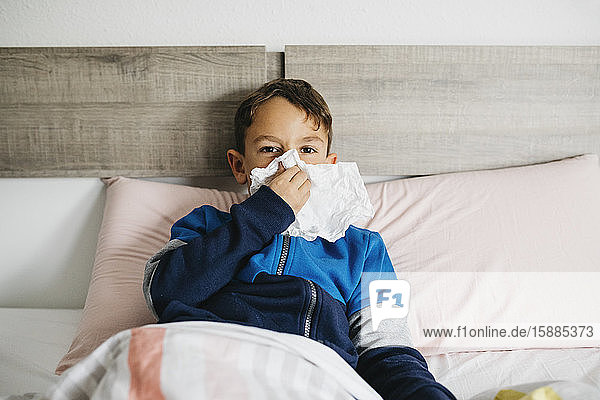 Porträt eines kranken Jungen  der im Bett liegt und sich die Nase schnäuzt