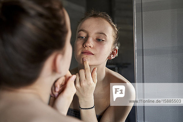 Mirror image of girl applying face cream in bathroom