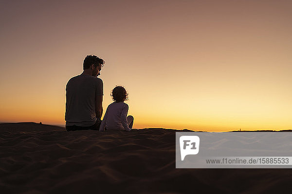 Father sitting with daughter in sand dunes at sunset  Gran Canaria  Spain