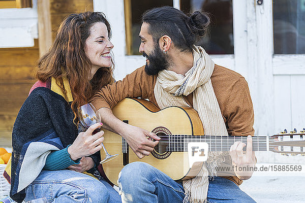 Paar  das auf der Gitarre Musik spielt und Wein vor einer Hütte auf dem Land trinkt