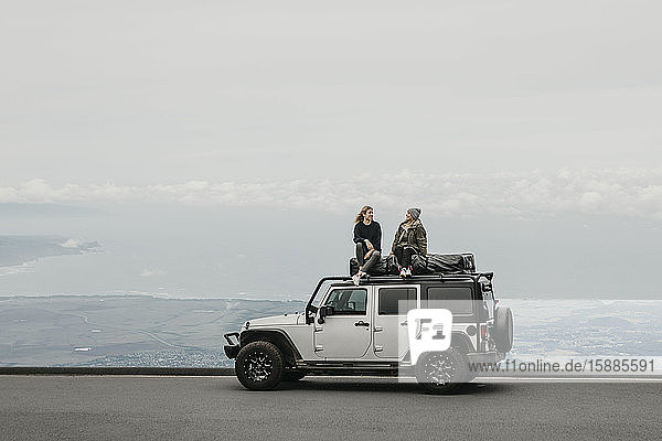 Friends talking while sitting on top of SUV at Maui Hawaii USA