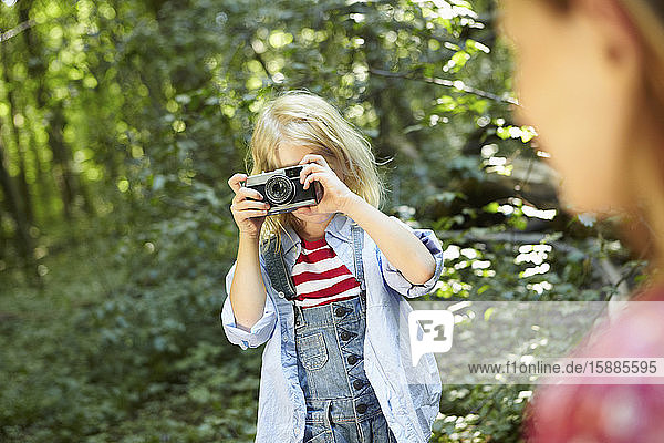 Girl taking picture in forest with old-fashioned camera