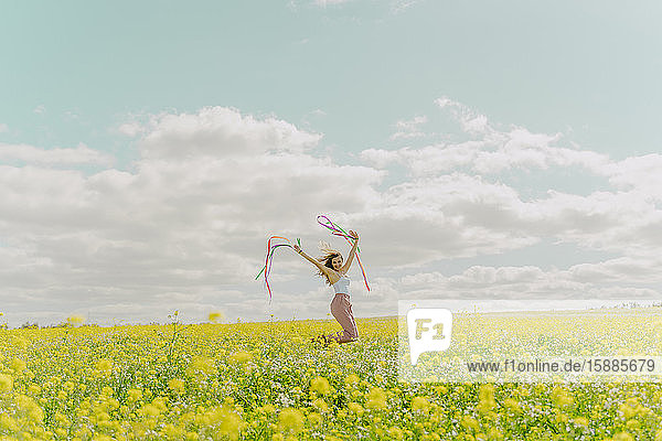 Glückliche junge Frau bewegt sich im Frühling mit bunten Bändern auf einer Blumenwiese