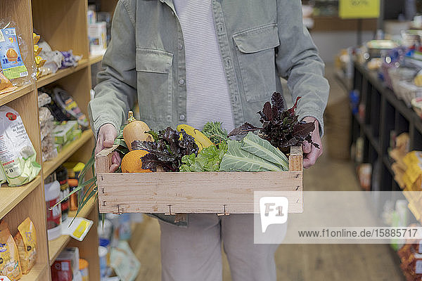 Nahaufnahme eines älteren Mannes  der in einem kleinen Lebensmittelgeschäft eine Kiste mit Gemüse trägt