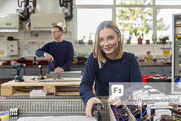 Porträt einer lächelnden Elektrikerin  die in einer Werkstatt an Schaltkreisen arbeitet