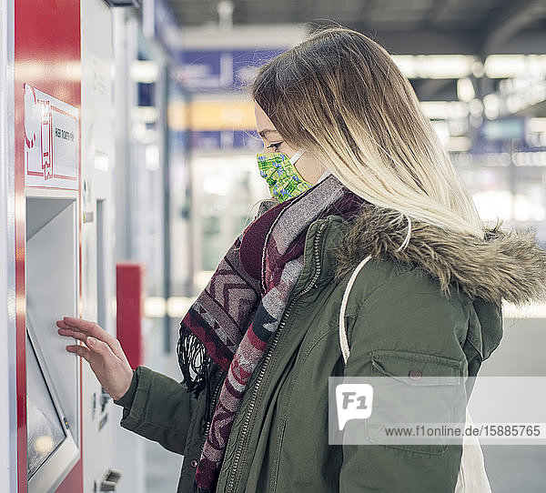 Junge Frau mit Maske am Fahrkartenautomaten am Bahnhof