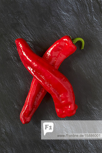 Two red chili peppers on black stone surface