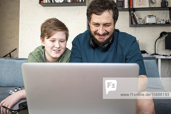 Porträt von Vater und Sohn  die zusammen auf der Couch sitzen und einen Laptop benutzen