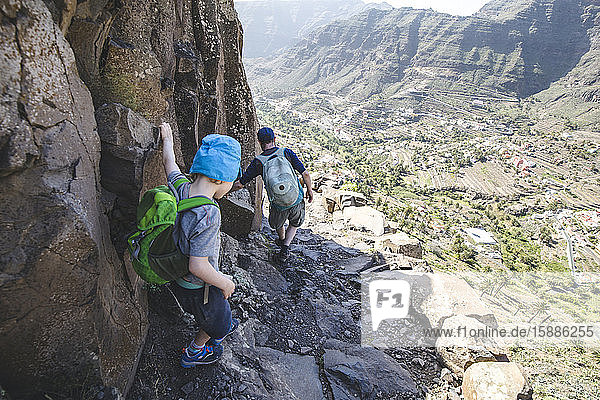 Back view of father and little son with backpacks on a hiking trail in the mountains  La Gomera  Canary Islands  Spain