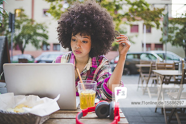 Junge Frau mit Afrofrisur mit Laptop in einem Straßencafé in der Stadt
