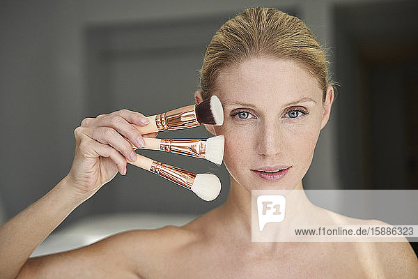 Portrait of beautiful woman holding assortment of beauty brushes