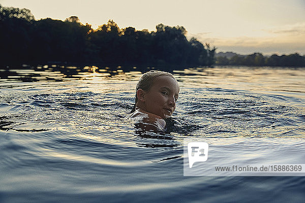 Mädchen schwimmt in der Abenddämmerung in einem See