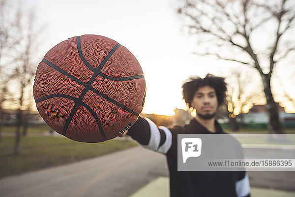 Junger sportlicher Mann posiert bei Sonnenuntergang mit Basketball auf dem Platz