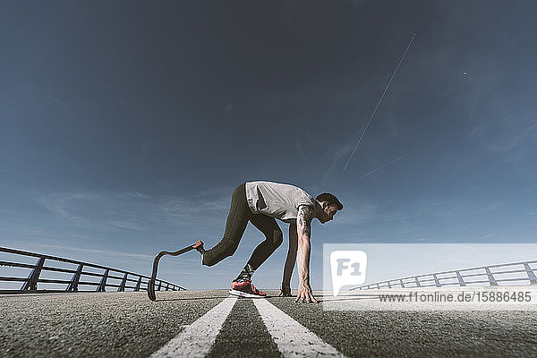 Disabled athlete with leg prosthesis in starting position on a road