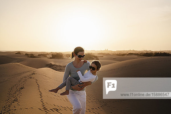Mother carrying daughter in sand dunes at sunset  Gran Canaria  Spain