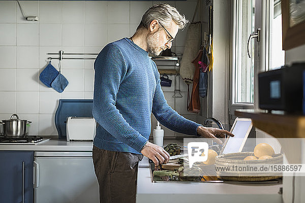 Reifer Mann bereitet Artischocken in seiner Küche mit Hilfe einer digitalen Tablette zu