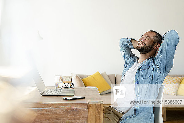 Junger Mann arbeitet zu Hause an seinem Laptop im Home-Office und macht eine Pause