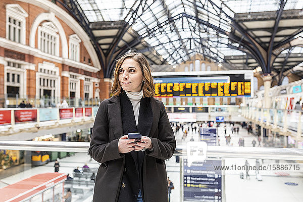 Frau am Bahnhof mit einem Mobiltelefon in der Hand  London  UK