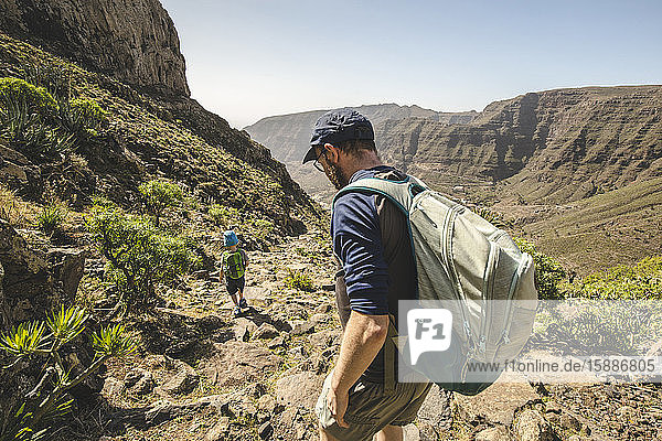 Father and little son with backpacks walking on a hiking trail in the mountains  La Gomera  Canary Islands  Spain