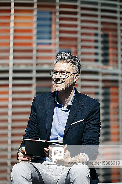 Happy businessman with tablet and cell phone in the city