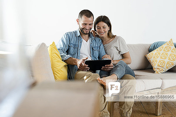 Glückliches Paar zu Hause im modernen Wohnzimmer auf der Couch sitzend  während sie gemeinsam auf die Tafel schauen