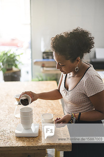 Frau  die in einer Kaffeerösterei arbeitet und Kaffeebohnen in eine Tasse gießt