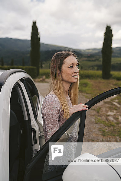 Lächelnde junge Frau steigt in ländlicher Landschaft aus dem Auto  Toskana  Italien