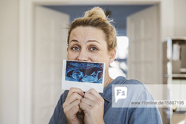 Portrait of pregnant woman showing ultrasound image at home
