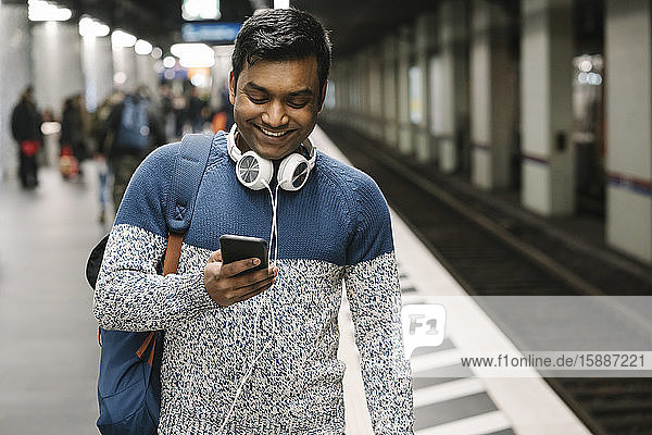 Lächelnder Mann benutzt Smartphone in U-Bahn-Station