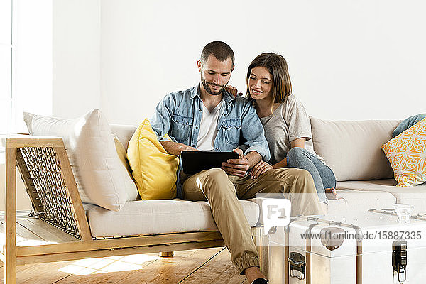 Lächelndes Paar zu Hause im modernen Wohnzimmer auf der Couch sitzend  während sie gemeinsam auf die Tafel schauen