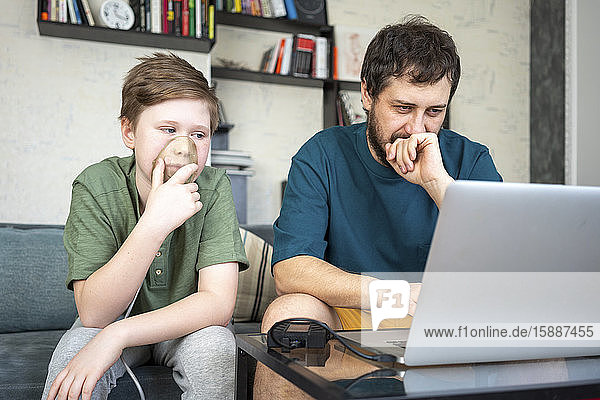 Portrait of father and son sitting together on the couch using laptop
