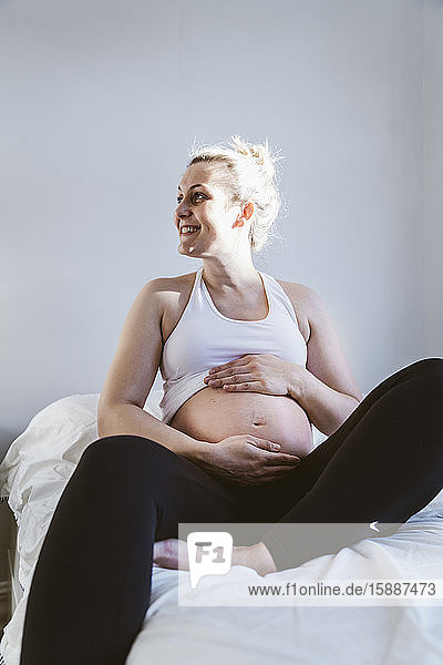 Glückliche schwangere Frau sitzt zu Hause auf dem Bett
