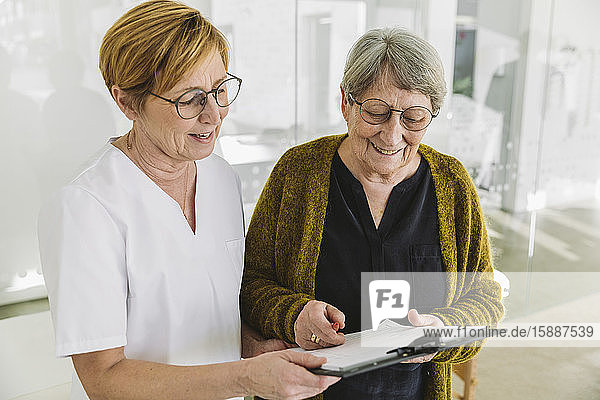Medizinische Sekretärin hilft älterem Patienten beim Ausfüllen des Dokuments