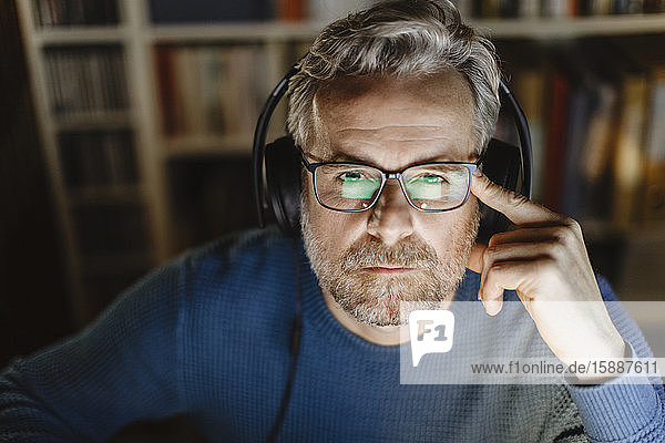 Portrait of pensive mature man with headphones in front of computer