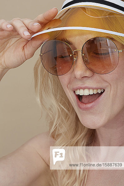Porträt einer glücklichen jungen Frau mit Sonnenbrille und Sonnenblende