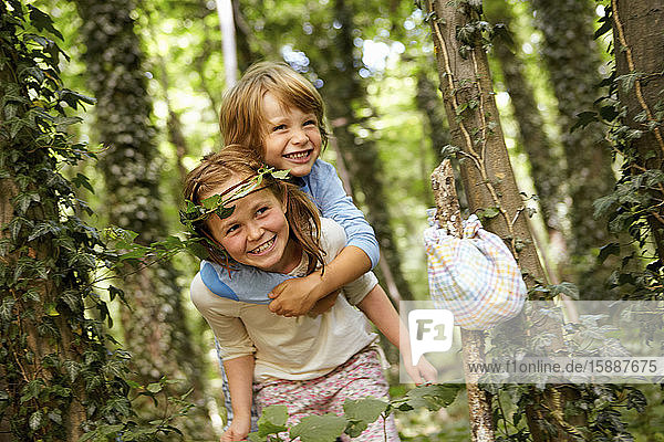 Girl carrying boy piggyback in forest