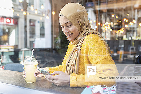 Portrait of young woman with smoothie and smartphone in a cafe
