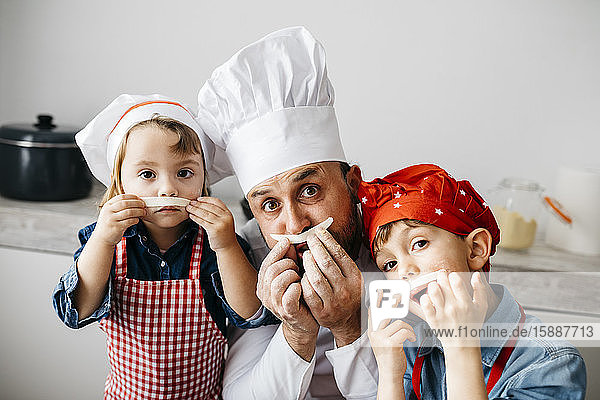 Verspielter Vater mit zwei Kindern  der sich beim Zubereiten von hausgemachter Pasta in der heimischen Küche amüsiert