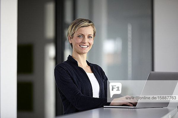 Porträt einer lächelnden Geschäftsfrau mit Laptop im Büro