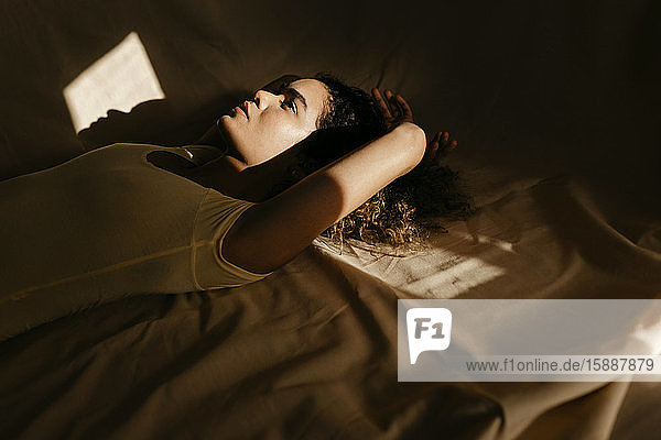 Porträt einer attraktiven jungen Frau  die im Bett im Sonnenlicht liegt