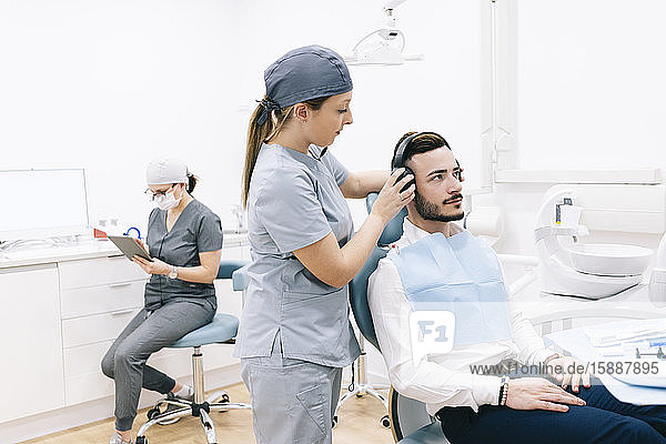 Medizinische Sekretärin bereitet Zahnbehandlung vor  setzt Kopfhörer auf den Kopf des Patienten auf