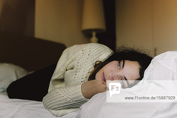 Portrait of pensive girl lying on bed looking at distance
