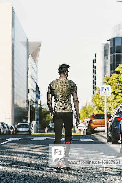 Rear view of disabled athlete with leg prosthesis walking on a street in the city